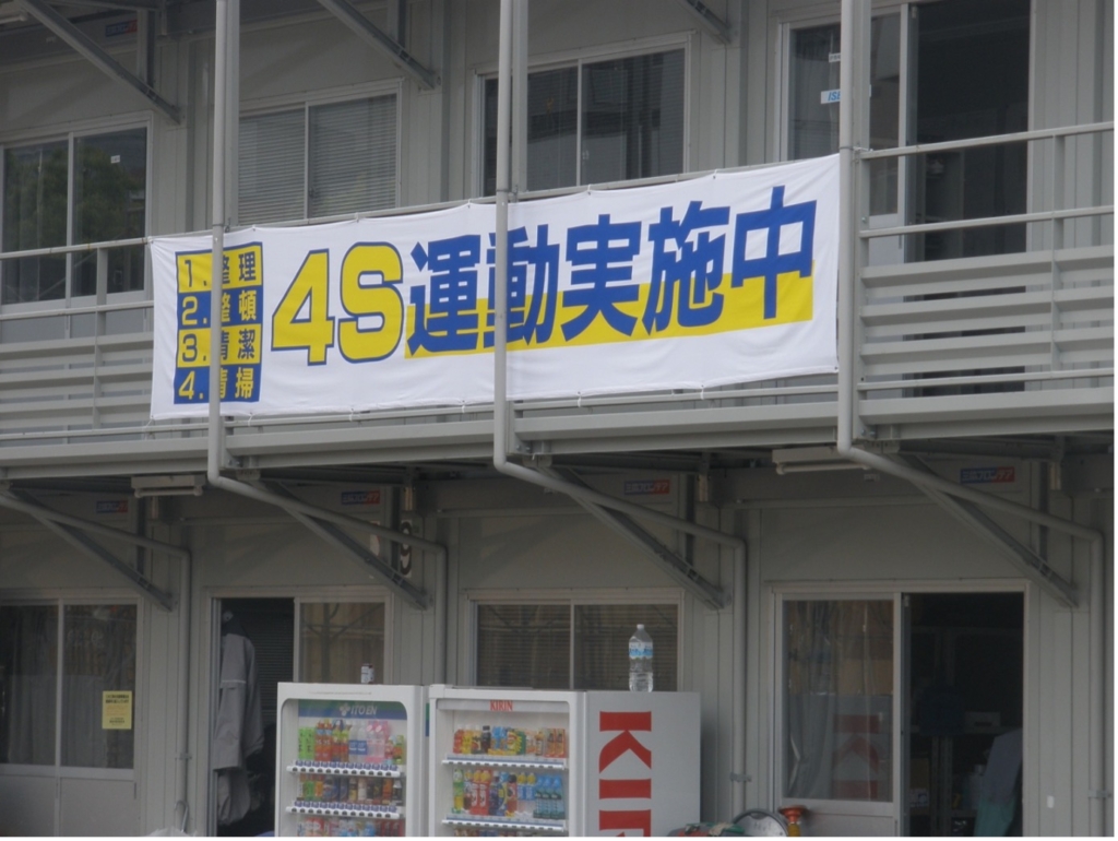 Foto van een Japanse banner die de '4S' methode promoot, opgehangen aan een gebouw, met genummerde stappen in het Japans, wat wijst op een lokale versie van de 5S-methodologie voor werkplekorganisatie.